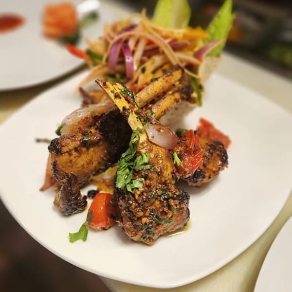 Indian lamb chops with red onions, tomatoes, and cilantro on a white plate.