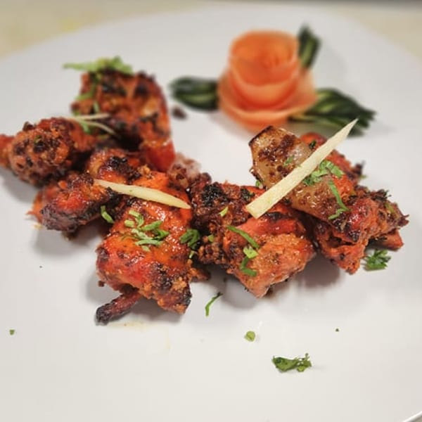 Clay Pit's Indian chicken tikka, garnished with fresh cilantro and ginger, on a white plate.