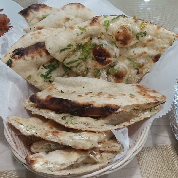 A basket of freshly baked Indian naan bread, some topped with herbs and garlic, others stuffed with cheese.