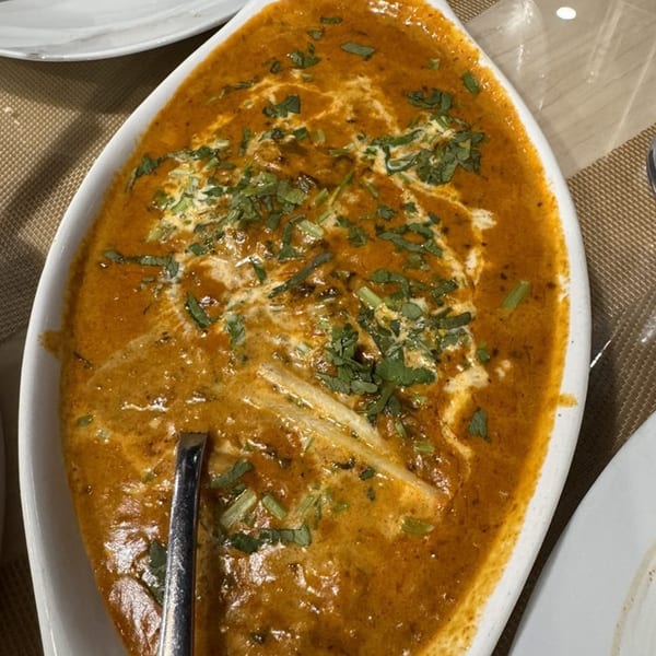 A white oval dish filled with Clay Pit's creamy orange Indian curry, garnished with fresh herbs.